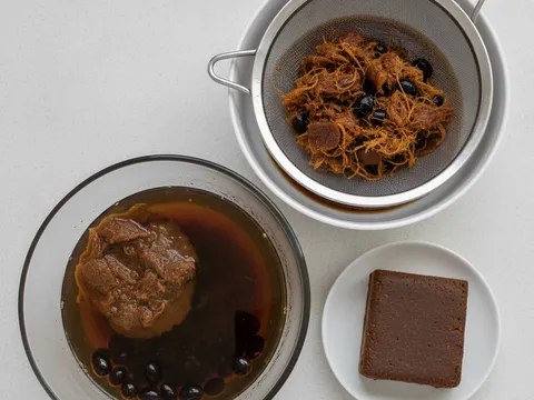 Asam jawa berbiji direndam dalam mangkuk air suam, isinya sudah terurai dan airnya bertukar perang pekat