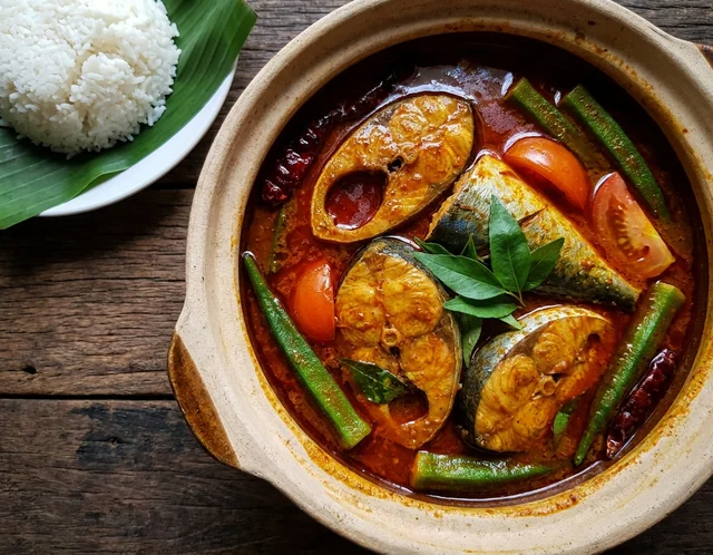 Asam Pedas Ikan Malaysia kuah merah tua pekat berkilat dengan ikan tenggiri, bendi hijau, tomato merah dan daun kesum dalam periuk tanah