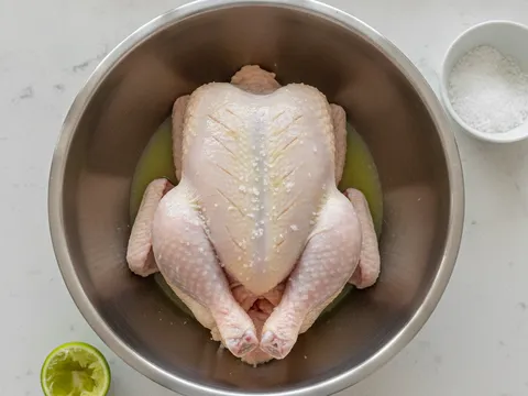 Ayam utuh dalam besen dilumur jus limau nipis dan garam, permukaannya dicucuk dengan garpu