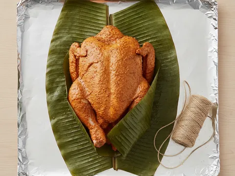 Ayam berempah dibalut rapat dengan daun pisang bertindih di atas kerajang aluminium yang terbentang
