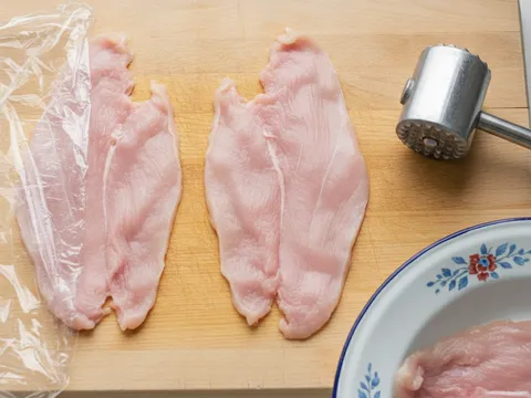 Dada ayam dibelah butterfly dan diketuk nipis di bawah lapisan plastik di atas papan pemotong