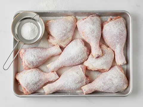 Ketulan ayam digolek dalam tepung jagung di atas dulang sehingga bersalut nipis dan sekata