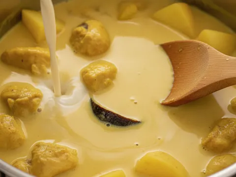 Santan cair dituang ke dalam periuk ayam berpes kuning bersama kentang dan asam keping