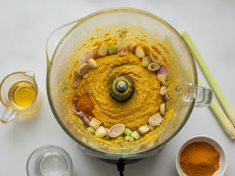 Bawang besar, bawang merah, bawang putih, halia dan serai dikisar menjadi pes perapan kuning pekat dalam pengisar