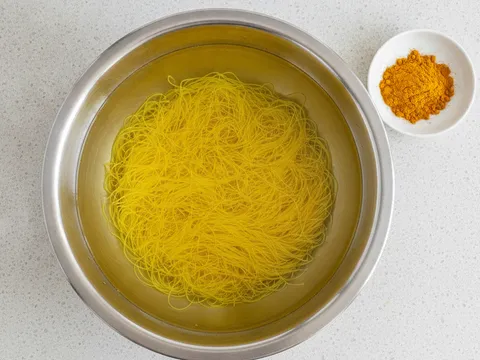 Bihun kering direndam dalam besen berisi air bercampur serbuk kunyit sehingga bertukar warna kuning
