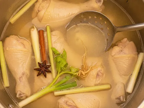 Potongan ayam berempah direneh dalam periuk besar berisi kuah sup jernih bersama batang daun sup