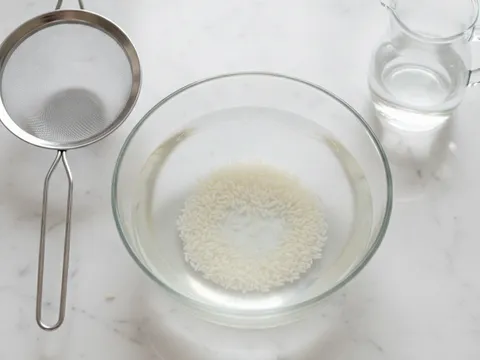Beras putih dicuci dalam mangkuk kaca dengan air jernih sebelum ditos untuk dimasak menjadi bubur