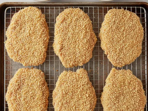 Keping ayam ditekan ke dalam serbuk roti sehingga bersalut tebal sekata di atas dulang