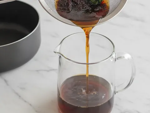 Air gula perang gelap dituang melalui penapis halus ke dalam jag kaca untuk disejukkan