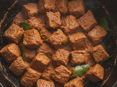 Kiub daging lembu digaul bersalut pes kari merah gelap di dalam periuk