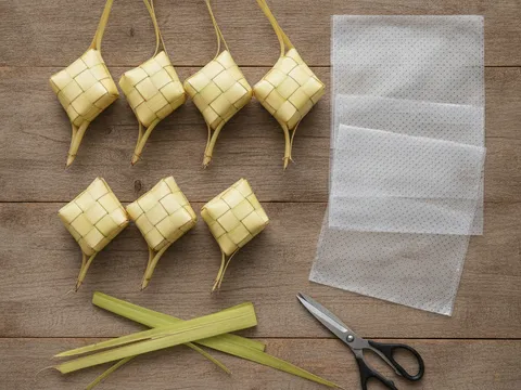 Sarung ketupat anyaman daun kelapa muda kosong disusun bersebelahan uncang plastik ketupat