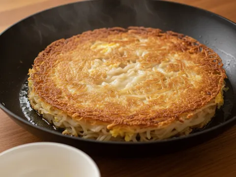 Kuey teow bersalut telur digoreng seperti satu keping dalam kuali sehingga tepinya garing keemasan