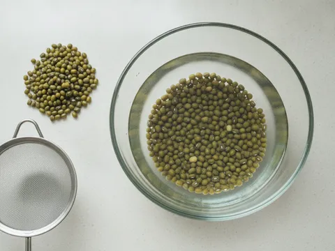 Kacang hijau kering direndam dalam mangkuk berisi air jernih di atas meja dapur