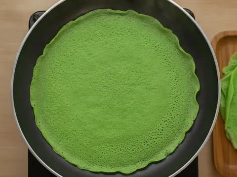 Kulit dadar hijau nipis dimasak dalam kuali leper non-stick dengan tepi mula terangkat