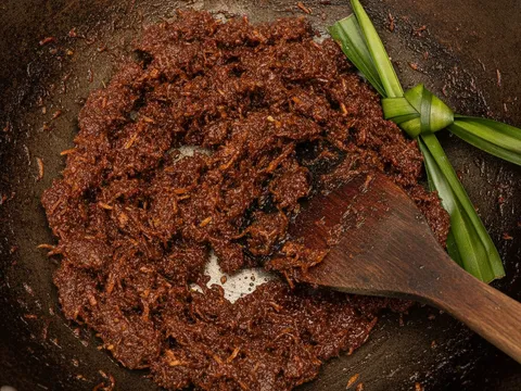 Inti kelapa gula melaka berwarna coklat keemasan dimasak dalam kuali sehingga pekat dan kering
