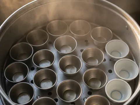 Acuan kuih lompang kecil disapu minyak dan disusun dalam kukusan berwap untuk dipanaskan