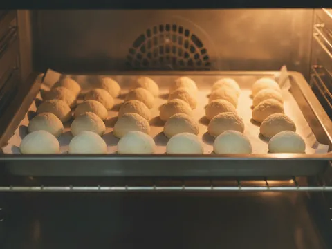 Kuih makmur berbentuk bujur berwarna pucat gading disusun di atas loyang dalam ketuhar