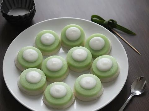 Kuih nona manis hijau berinti putih tersusun di atas pinggan, acuan lompang kosong dan pangkal sudu teh di sisi