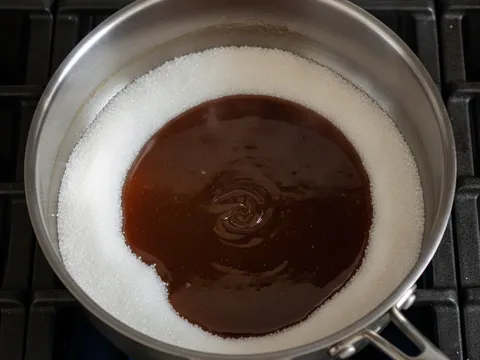 Gula pasir cair menjadi karamel berwarna perang gelap di dalam periuk keluli di atas dapur
