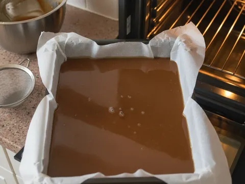 Adunan cair berwarna perang dituang ke dalam loyang berlapik kertas baking sebelum dimasukkan ke dalam ketuhar