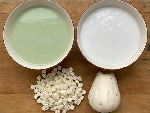 Dua mangkuk adunan kuih tako — adunan pandan hijau dan adunan santan putih — bersebelahan dengan sengkuang dadu di atas papan pemotong