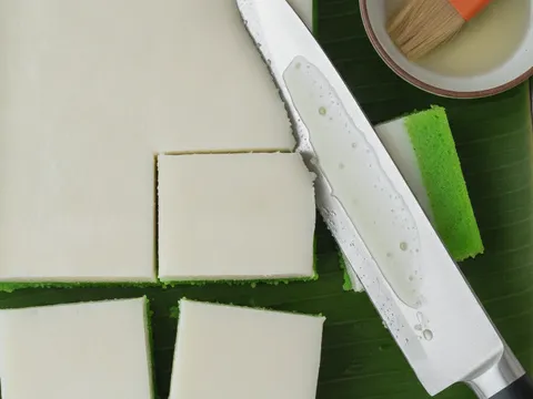 Kuih talam yang telah sejuk dipotong bentuk petak dengan pisau berminyak, menampakkan dua lapisan hijau dan putih yang kemas