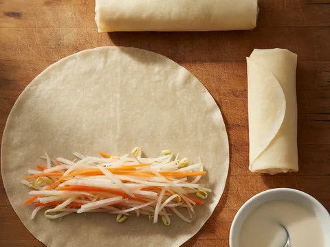 Sekeping kulit popia homemade sedang digulung bersama inti sayur di atas papan pemotong
