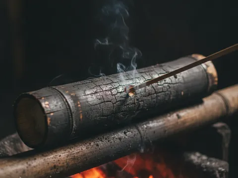 Buluh lemang hangus kecoklatan diangkat dari bara untuk diuji kematangannya dengan lidi