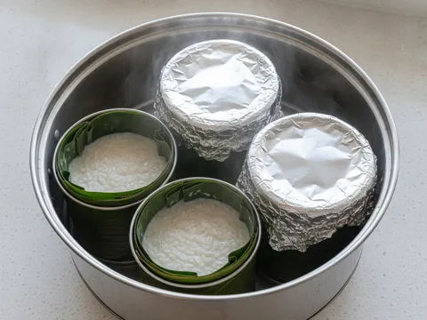 Tin aluminium berlapik daun pisang berisi pulut dan santan disusun dalam kukusan sebagai lemang versi rumah