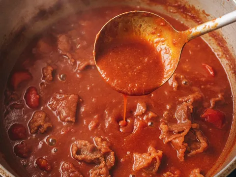 Kuah mee bandung merah pekat direneh bersama hirisan daging rebus dalam periuk