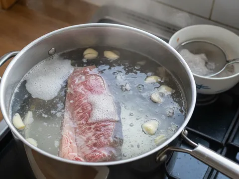 Daging lembu seketul direbus dalam periuk berisi air jernih bersama bawang putih dan bawang merah