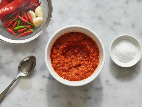Sambal lada merah kasar dalam mangkuk kecil di sebelah cili merah dan cili padi yang telah direbus