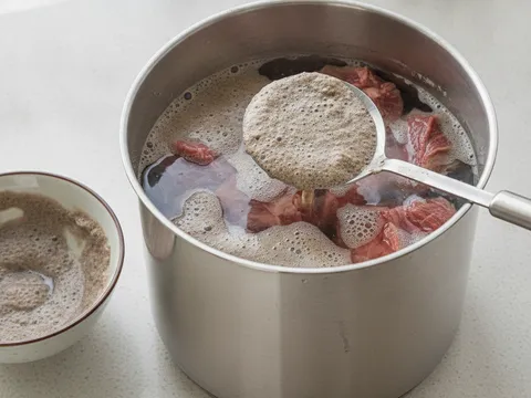 Ketul daging lembu dalam periuk air sejuk dengan buih kotor dibuang menggunakan senduk berlubang