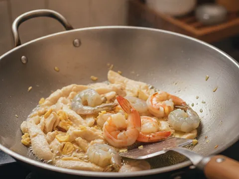 Hirisan ayam nipis dan udang dimasak bersama tumisan bawang putih dalam kuali, udang baru bertukar merah jambu