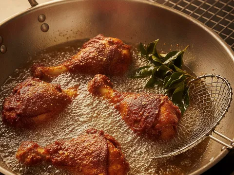 Ketulan ayam berempah bersalut tepung nipis digoreng bersama daun kari dalam minyak panas