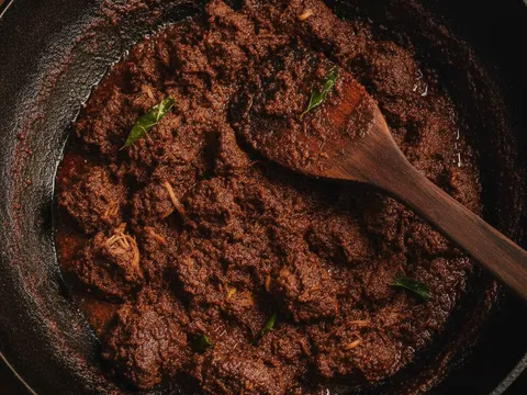 Rendang daging berwarna perang gelap yang pekat berminyak dikacau dengan senduk kayu dalam kuali