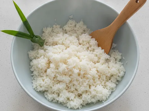 Nasi putih berderai digemburkan dengan senduk kayu dalam mangkuk besar untuk disejukkan