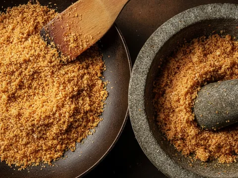 Kelapa parut digoreng tanpa minyak sehingga keperangan kemudian ditumbuk kasar dalam lesung batu