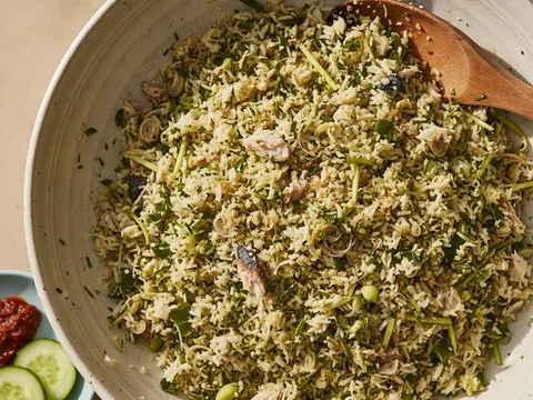 Nasi ulam digaul rata dengan tangan dalam mangkuk besar sehingga hirisan daun bertabur sekata