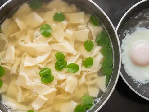 Mee koyak timbul di permukaan stok bersama sayur manis hijau, dengan telur separuh masak dipoach dalam kuali air berasingan