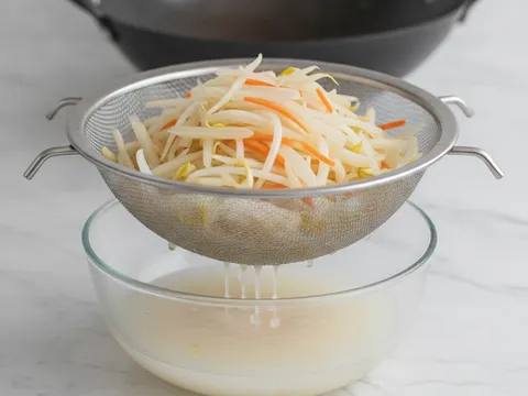 Inti popiah ditapis dalam penapis besi di atas mangkuk, air jus sayur menitis ke bawah