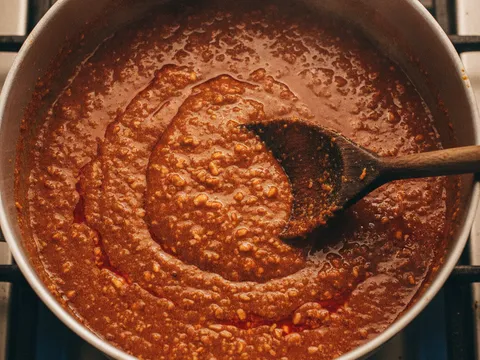 Kuah kacang coklat pekat dimasak dalam periuk dengan minyak naik ke permukaan, dikacau dengan senduk kayu