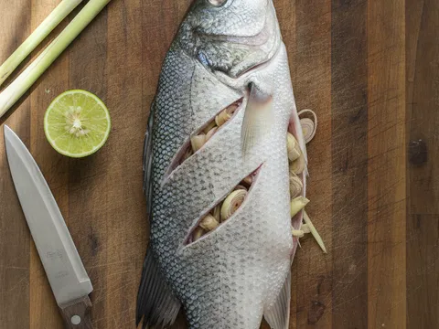 Ikan siakap dikelar tiga kali senget pada badannya, dengan potongan serai yang telah diketuk disumbat ke dalam perutnya