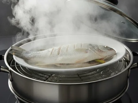 Ikan siakap di atas pinggan dalam periuk pengukus yang berwap tebal, penutup diangkat sedikit