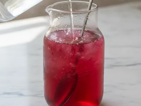 Air sejuk dituang ke dalam jag berisi sirap ros dan dikacau dengan sudu panjang sehingga warna merah jambu menjadi sekata