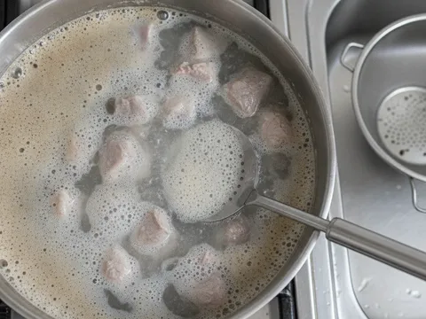 Ketulan daging lembu direbus sekejap dalam periuk dan buih di permukaan air rebusan pertama
